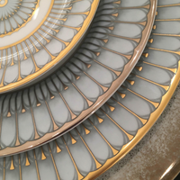 Close-up of three stacked Arcades Gold Dinnerware plates by Philippe Deshoulieres, showcasing gray and gold concentric patterns on fine Limoges porcelain with white centers and gold-rimmed edges for a refined, symmetrical finish.