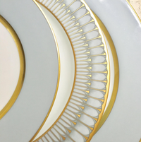 Close-up of Recamier Grey & Gold Dinnerware by Royal Limoges—elegant French porcelain dinner plates with gold rims and detailed gold patterns, stacked together for a sophisticated look.