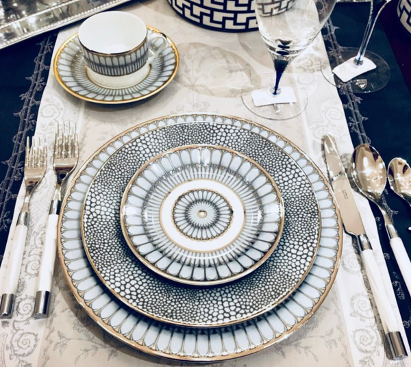 Elegant table setting featuring a Makassar Gold Dinnerware plate trio by Royal Limoges, matching cup and saucer, white-handled cutlery, and a wine glass on a decorative placemat, arranged for a formal meal.