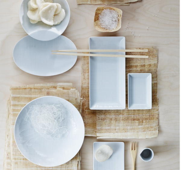 A minimalist table setting with Rosenthal Mesh Dinnerware White—white plates, bowls, and rectangular porcelain dishes—plus chopsticks, a wooden fork, rice noodles, prawn crackers, soy sauce, and salt on light wood. All pieces are dishwasher safe.