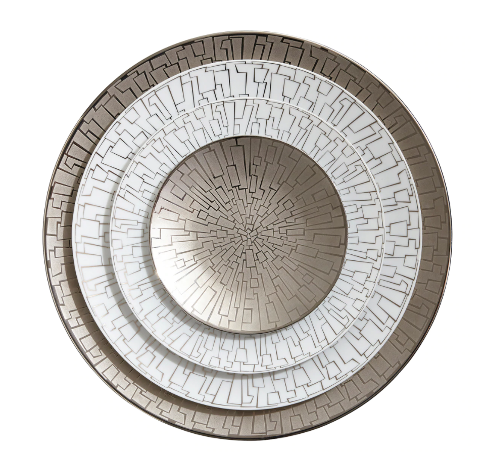 The Rosenthal Skin Platinum TAC 02 Dinnerware set features four nested porcelain plates with intricate geometric platinum and white designs, creating concentric circles that resemble a maze or circuit board radiating from the center.