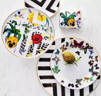 Two porcelain dessert plates and a cup with colorful floral, leaf, butterfly, and bold black geometric designs on white—part of the elegant Primavera Serving Pieces by Vista Alegre.