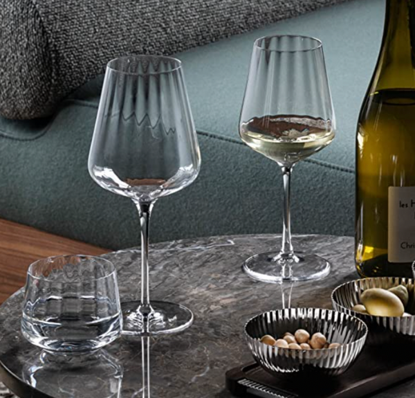 A Georg Jensen Bernadotte Glassware Set of 6 sits on a round marble table with a wine bottle and snack bowls, while a green sofa is visible in the background.
