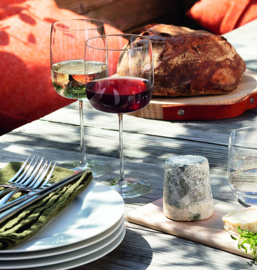 Two glasses of wine—one red, one white—served in the LSA Borough Barware Set of 4 rest on an outdoor table with rustic bread, blue cheese, plates, utensils atop a green napkin, and a glass of water.