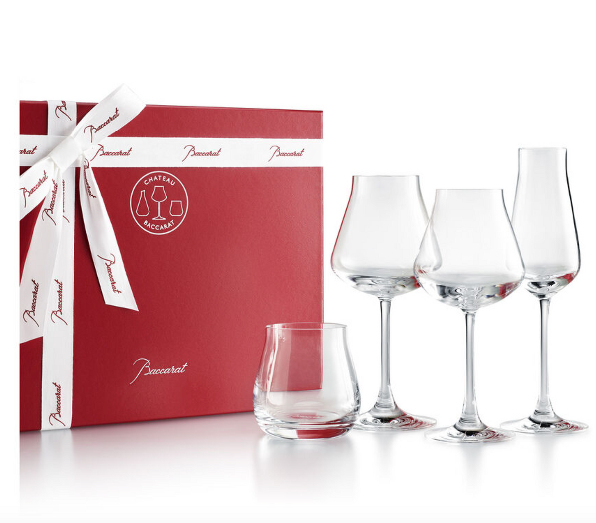 A red gift box with white ribbon sits beside four Baccarat Chateau Barware crystal glasses—one tumbler and three wine glasses—arranged on a white background. Each expertly crafted piece is made in France.