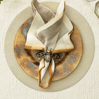 A beige and brown napkin with a bee ring sits on a rustic plate, all placed atop the Kim Seybert Pebble Placemats Set of 4 on a light tablecloth.