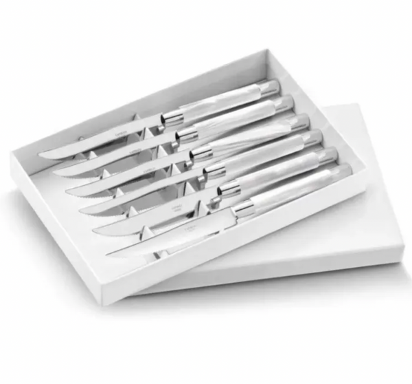 The Capdeco Conty Steak Knives Set of 6 features stainless steel knives with shiny metal handles, neatly aligned side by side in a white box with the lid partially open.