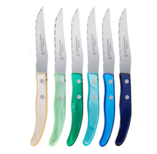 The Claude Dozorme Berlingot Blue & Green Steak Knives Set of 6 features serrated stainless steel blades and shiny handles in white, green, teal, light blue, dark blue, and turquoise, all made in France and arranged upright side by side.