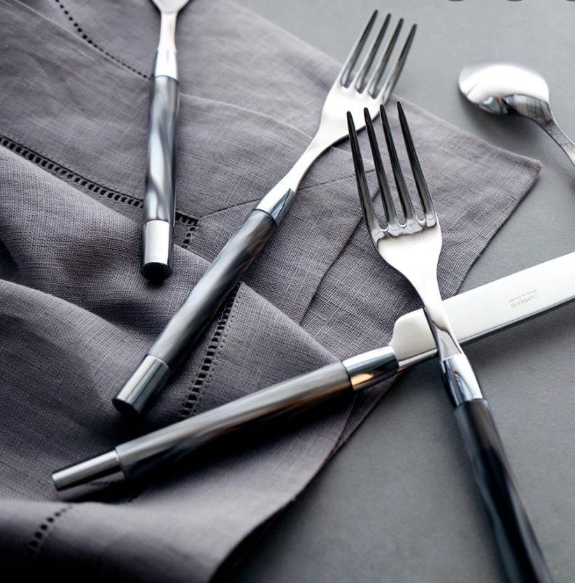 A set of six Capdeco Conty steak knives with dark handles is arranged on a folded gray napkin atop a gray surface.