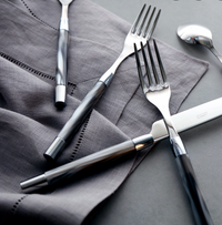 A set of six Capdeco Conty steak knives with dark handles is arranged on a folded gray napkin atop a gray surface.