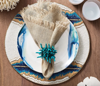 A table setting featuring Kim Seybert’s Fringe Napkin Silver & Natural Set of 4 on a blue and white plate with a beaded placemat, turquoise coral napkin ring, white bowls, and decor atop a wooden table.