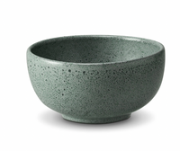 The Terra Seafoam Dinnerware by L'Objet is a green, speckled ceramic bowl with a rounded shape, shown on a white background, showcasing the craftsmanship of artisanal tableware.
