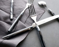 A close-up of the Capdeco Conty Large Serving Spoon Grey, French-made from stainless steel, with a dark glossy handle, arranged on a gray cloth napkin atop a gray surface.