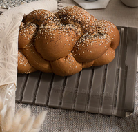 A braided challah topped with sesame and poppy seeds rests on a patterned cloth atop the Apeloig Personalized Solid Acrylic Challah Board, displayed on a textured table.