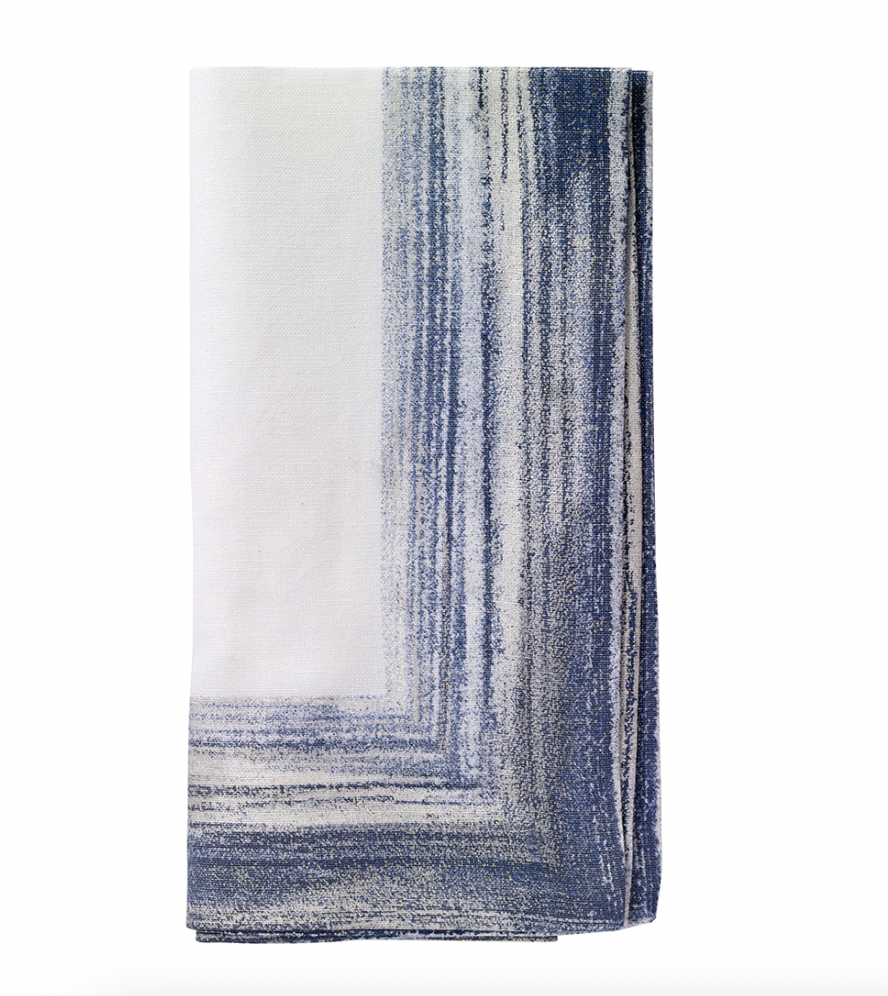 The Bodrum Cornice Napkin Navy Set of 4 features folded white cotton-linen napkins with an abstract navy and gray painterly border design on one corner, displayed against a plain white background.