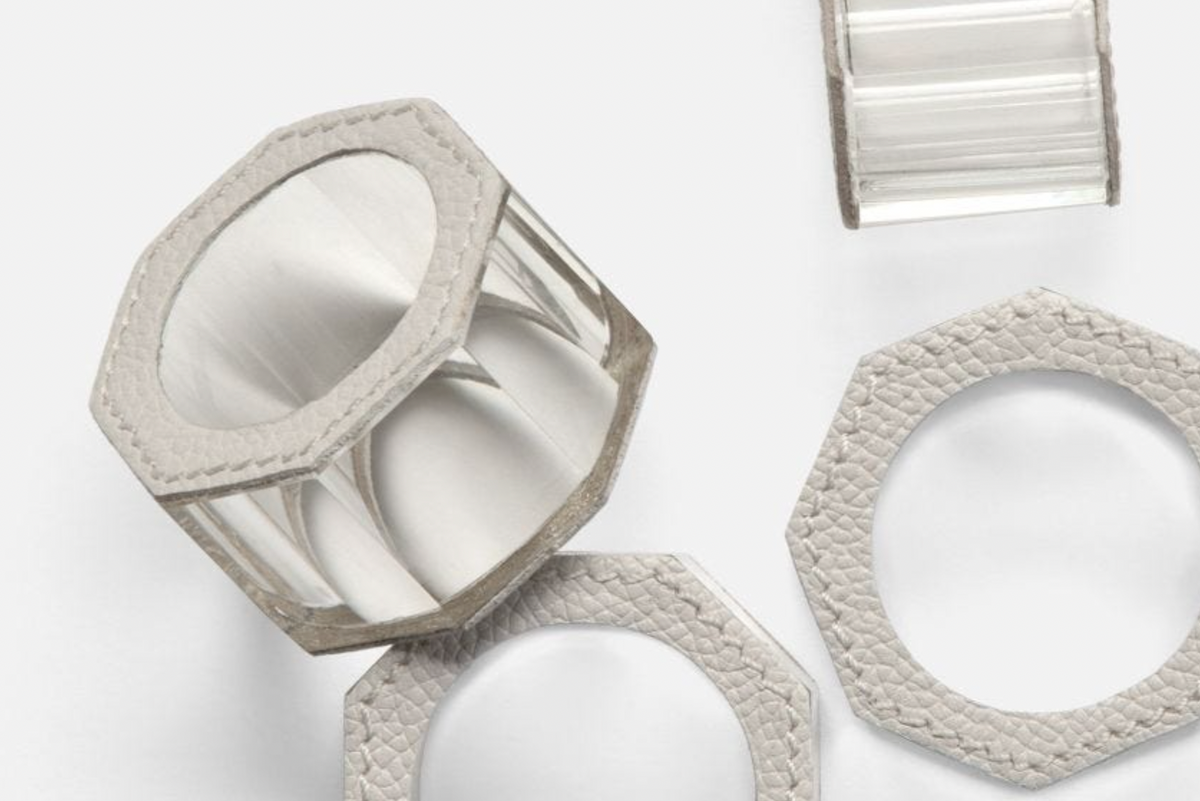 The Arthur Leather Grey Napkin Ring Set of 4 by Blue Pheasant showcases hexagonal clear and textured gray crystal napkin rings with leather-like borders, elegantly arranged to highlight their detailed design and luxury table decor appeal.
