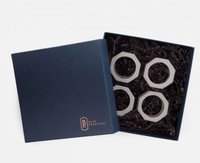 A navy Blue Pheasant box sits open, revealing four Arthur Leather Grey napkin rings nestled in black crinkle paper—a touch of luxury table decor for any setting.