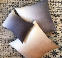 The Johanna Howard Dip Dye Pillow in Light Grey is arranged with two other gradient-toned pillows on a neutral, textured patterned rug.
