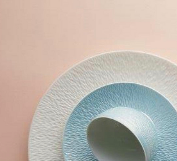 Raynaud's Mineral Irise Dinnerware Sky Blue set—featuring a textured white plate, smaller sky blue plate, and matching cup in fine Limoges porcelain—is stacked on pink, creating a soft and elegant color contrast.