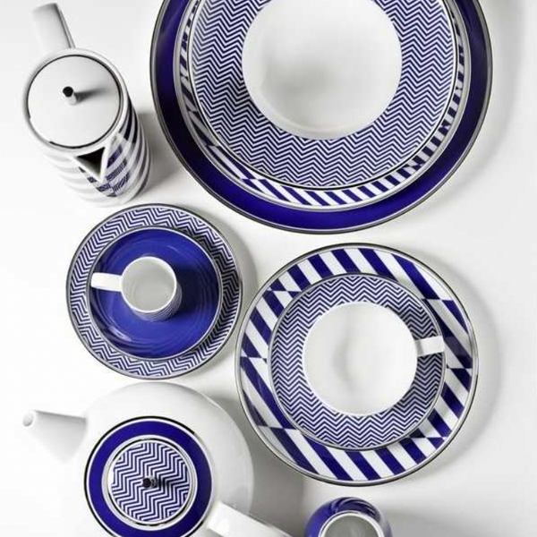 The Harvard Dinnerware set by Vista Alegre features bold blue and white geometric patterns on plates, cups, a teapot, and a tall pot. Made in Portugal, the pieces are arranged neatly on a white background.