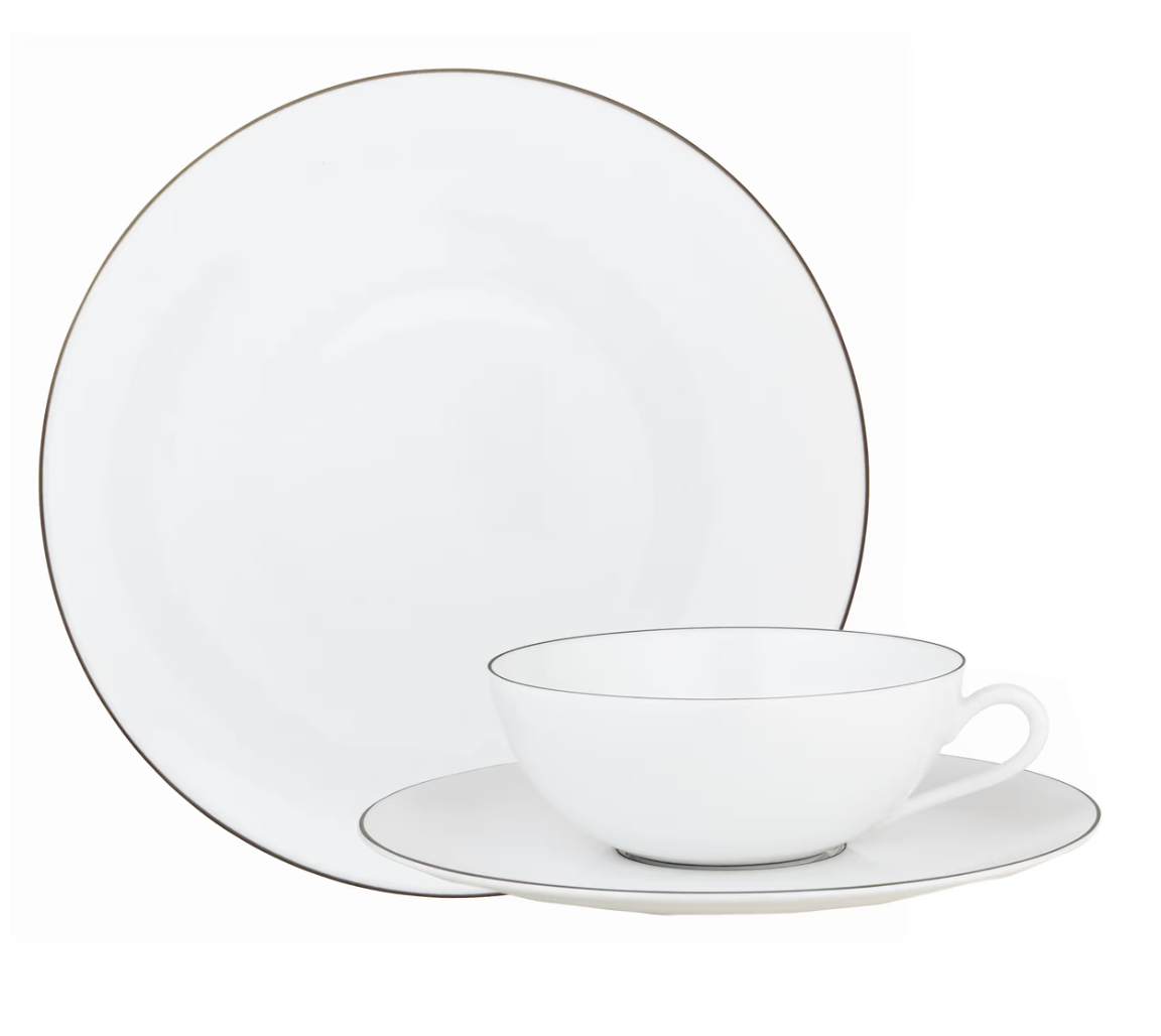 A Raynaud Monceau Oval Platter Platinum Large is placed behind a white Limoges porcelain teacup and saucer, all featuring thin platinum rims that beautifully showcase the refined elegance of Raynaud dinnerware.