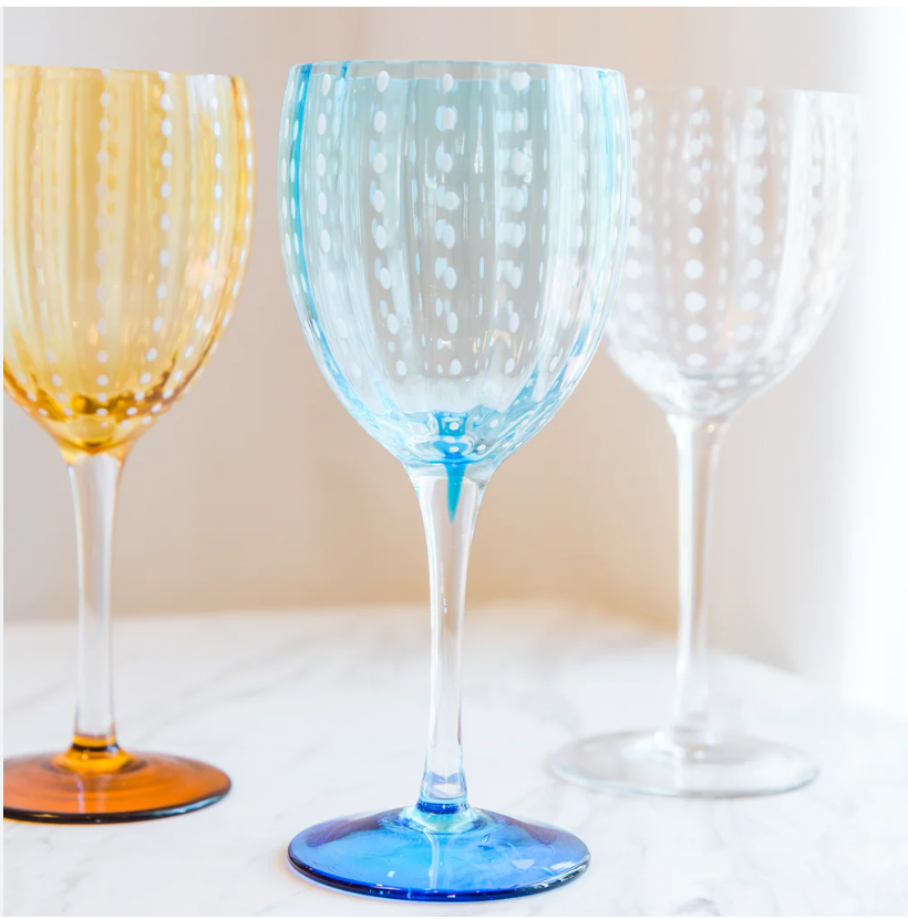A set of two Zafferano Perle Wine Goblets, featuring a dotted pattern in amber and blue, rests on white marble under soft natural light. Made in Italy, these elegant glasses are perfect for entertaining.