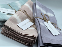 A set of four hand-dyed linen napkins in Dusty Rose by Whigstock Studio, each tied with twine and tagged, features subtle tie-dye patterns and sustainable style, arranged elegantly on a white surface.