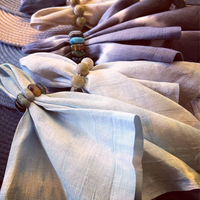 A close-up of Whigstock Studio's Hand Dyed Linen Napkin Set of 4 in Midnight, neatly arranged with napkin rings on a textured woven surface—sustainable essentials that add charm to any table setting.