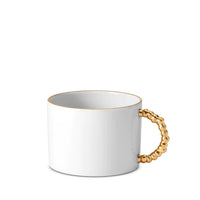 The Haas Mojave Dinnerware Gold mug by L'Objet is a white Fine Porcelain piece with a round body, thin gold rim, and a beaded gold handle. Inspired by Mojave Dinnerware, it is shown against a plain white background.