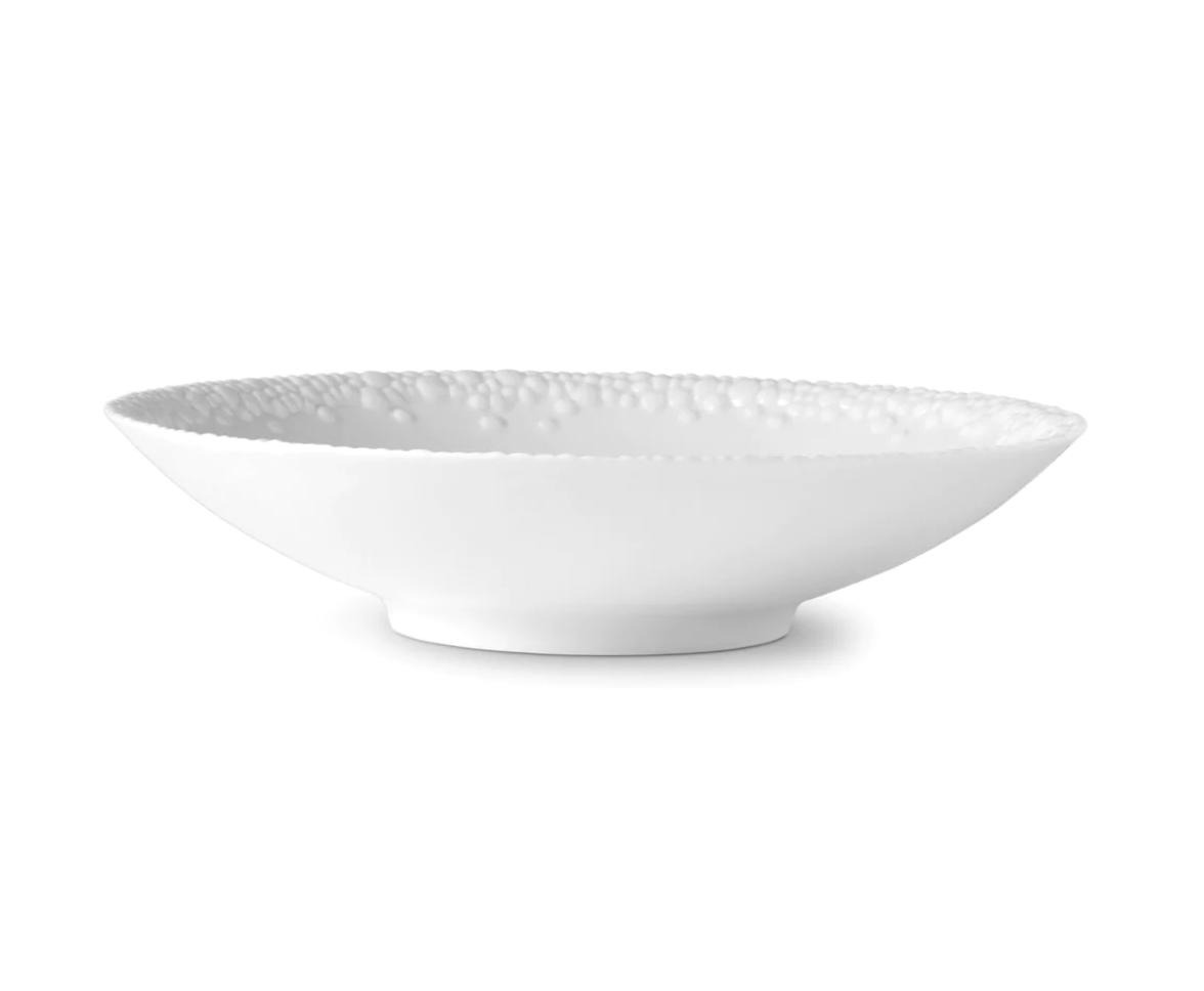 A shallow white ceramic bowl from L’Objet’s Haas Mojave White Dinnerware collection features a subtly raised base and textured dimpled inner rim, shown against a plain white background.