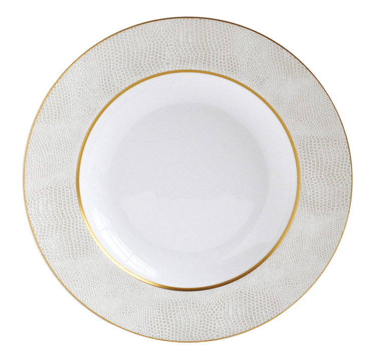 The Bernardaud Sauvage Gold Dinnerware features a white Limoges porcelain plate with a textured, light-patterned rim resembling embossed snake skin and finished with thin gold bands for an elegant, minimal design.