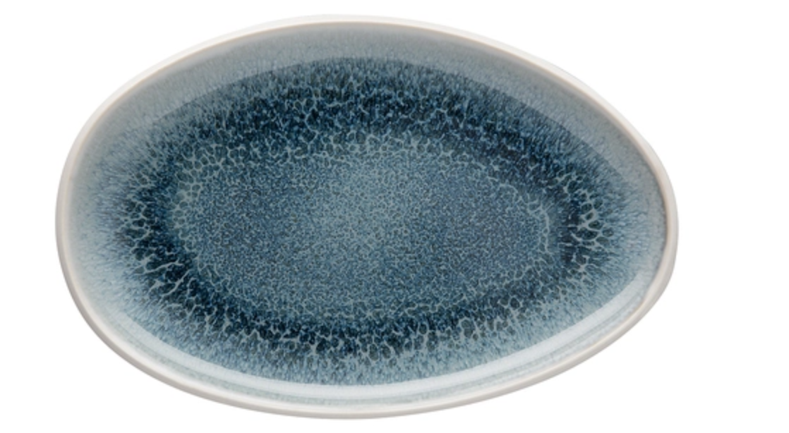 The Rosenthal Junto Aquamarine Dinnerware oval plate features a blue speckled reactive glaze interior with a smooth white rim. Made of stoneware, it's dishwasher and microwave safe. Plate is empty on a plain white background.
