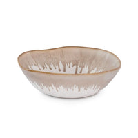 The Burlington Dinnerware Bluff by Simon Pearce is a shallow, round ceramic bowl with a light brown and white dripped glaze along the rim and an organically uneven edge.