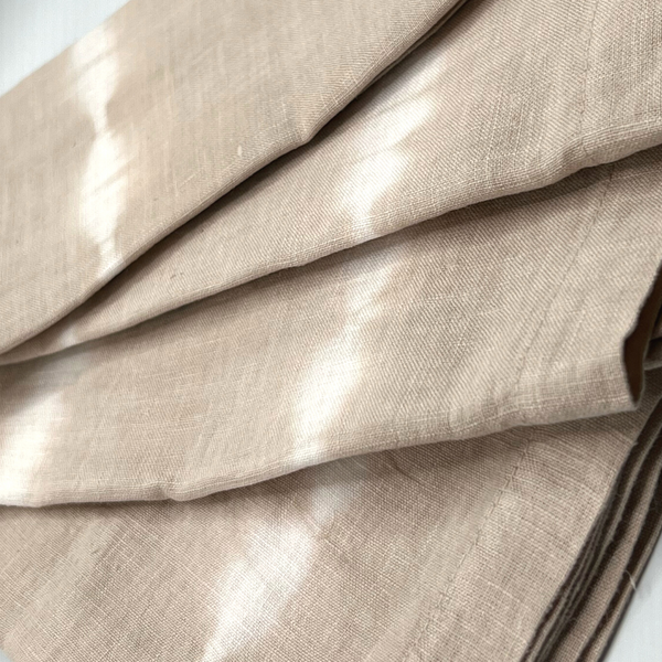 A close-up of Whigstock Studio’s Hand Dyed Linen Napkin Set of 4 in Bone highlights the subtle white tie-dye pattern, natural weave, and artisanal texture—an ideal sustainable essential for any home.