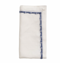 The Kim Seybert Filament Napkin White & Navy Set of 4 features neatly folded white linen napkins with blue embroidered borders, shown against a plain white background.