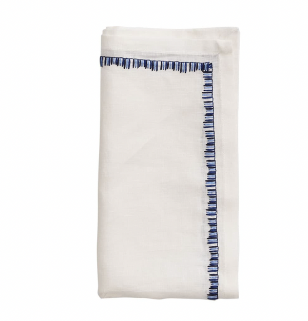 The Kim Seybert Filament Napkin White & Navy Set of 4 features neatly folded white linen napkins with blue embroidered borders, shown against a plain white background.
