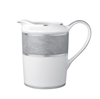 The Bernardaud Sauvage Grey & Platinum pitcher is crafted from white Limoges porcelain with a curved handle, pouring spout, platinum rim, and a textured snake skin-embossed platinum band, giving it a modern, elegant look.