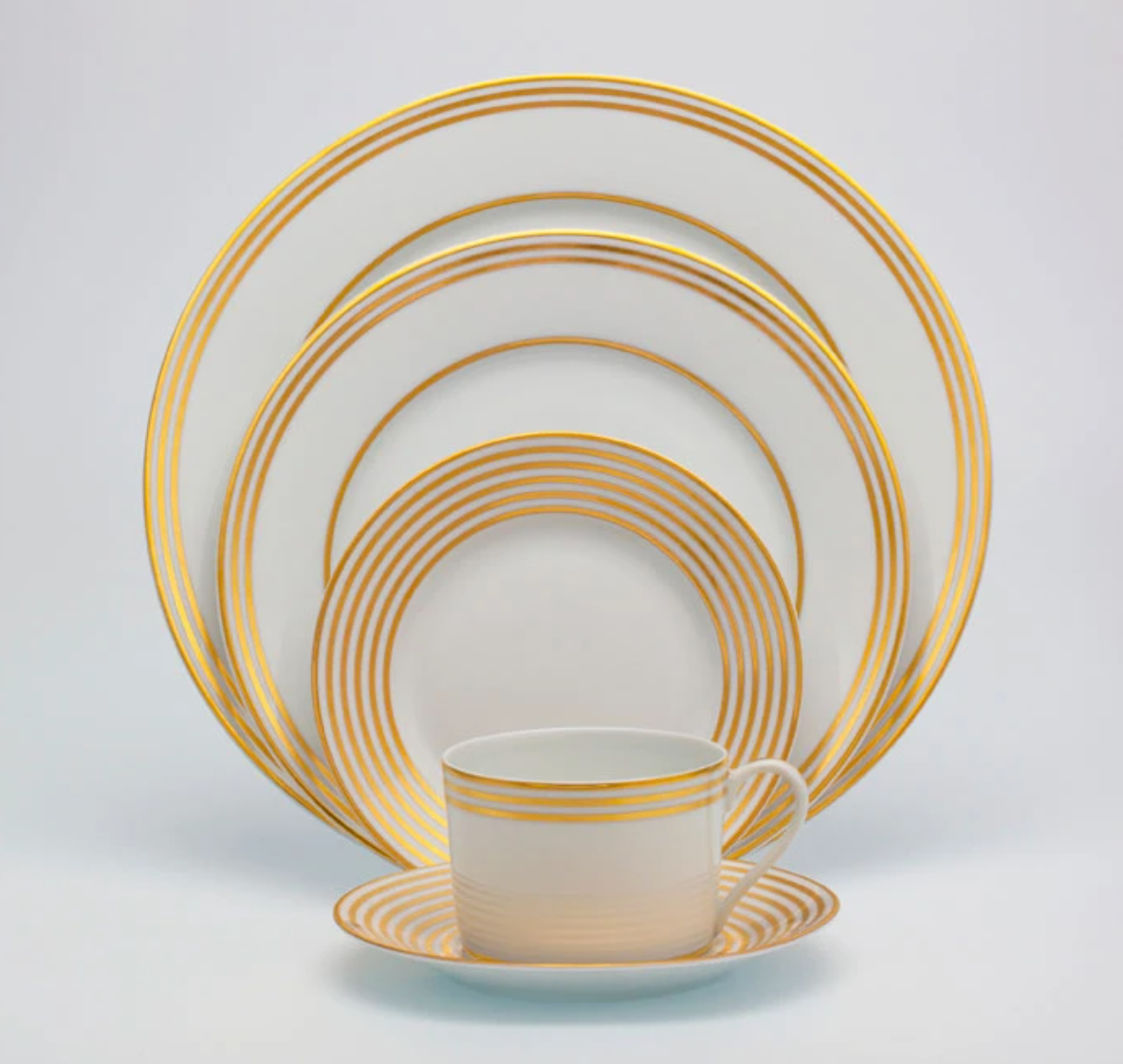 The Latitudes Dinnerware by Royal Limoges features fine porcelain with gold concentric circles, including four plates of various sizes and a teacup with matching saucer, all displayed neatly against a white background.