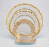 The Latitudes Dinnerware by Royal Limoges features fine porcelain with gold concentric circles, including four plates of various sizes and a teacup with matching saucer, all displayed neatly against a white background.