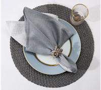 A Deborah Rhodes Metallic Two-Tone Silver placemat holds a gold-rimmed plate with a metallic linen napkin and jeweled ring; a transparent gold-rimmed glass sits beside it.