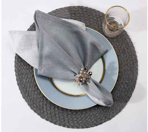 A Deborah Rhodes Metallic Two-Tone Silver placemat holds a gold-rimmed plate with a metallic linen napkin and jeweled ring; a transparent gold-rimmed glass sits beside it.