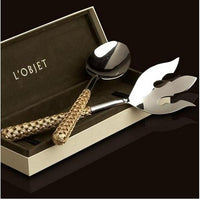 The Braid Serving Set Gold by L'Objet features a ladle and decorative fork with woven 24k gold plated handles, elegantly presented in an open L'Objet gift box against a dark backdrop.