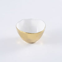The Moonlight Snack Bowl by PAMPA BAY is a small, round white porcelain bowl with a slightly uneven rim, glossy white interior, and shiny gold titanium exterior, shown on a plain white surface.