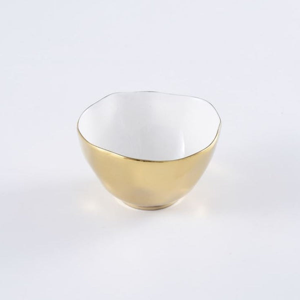 The Moonlight Snack Bowl by PAMPA BAY is a small, round white porcelain bowl with a slightly uneven rim, glossy white interior, and shiny gold titanium exterior, shown on a plain white surface.