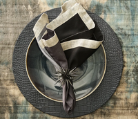 A dark gray plate rests on the Kim Seybert Croco Placemat Charcoal (Set of 4), paired with a two-tone napkin and a spiky napkin ring, all arranged on a rustic wooden table.