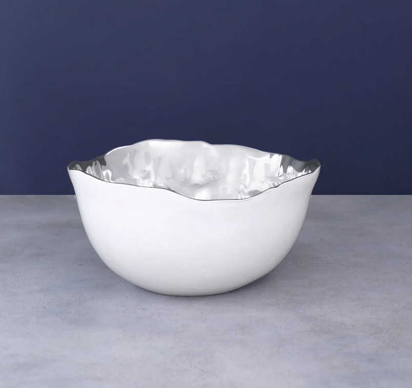 The Thanni Osaka Deep Bowl White and Silver Medium by Beatriz Ball, featuring a flower shape and wavy rim, sits on a light gray surface against a dark blue background.