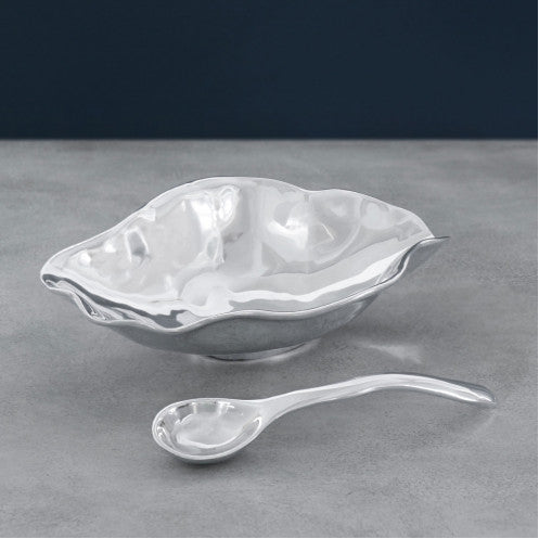 The Beatriz Ball Vento Claire Bowl With Spoon, an eco-friendly aluminum serving set with wavy edges and a modern reflective finish, sits on a gray surface—showcasing sustainable serveware design.