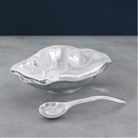 The Beatriz Ball Vento Claire Bowl With Spoon, an eco-friendly aluminum serving set with wavy edges and a modern reflective finish, sits on a gray surface—showcasing sustainable serveware design.