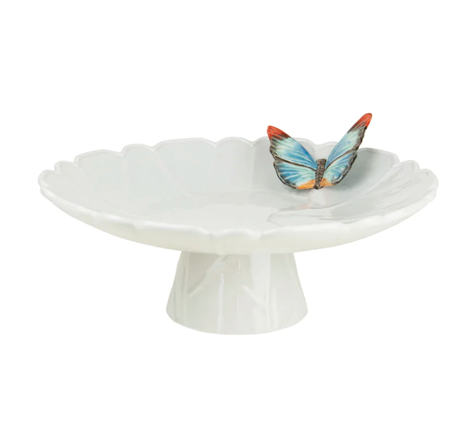 The Vista Alegre Cloudy Butterflies Cake Plate is a white earthenware dish with scalloped edges, adorned with a hand-painted blue and orange butterfly on the rim.