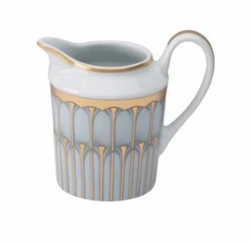 A porcelain cream pitcher from Philippe Deshoulieres' Arcades Gold Dinnerware, featuring a blue and white base, curved handle, and gold geometric arch patterns along the top edge.
